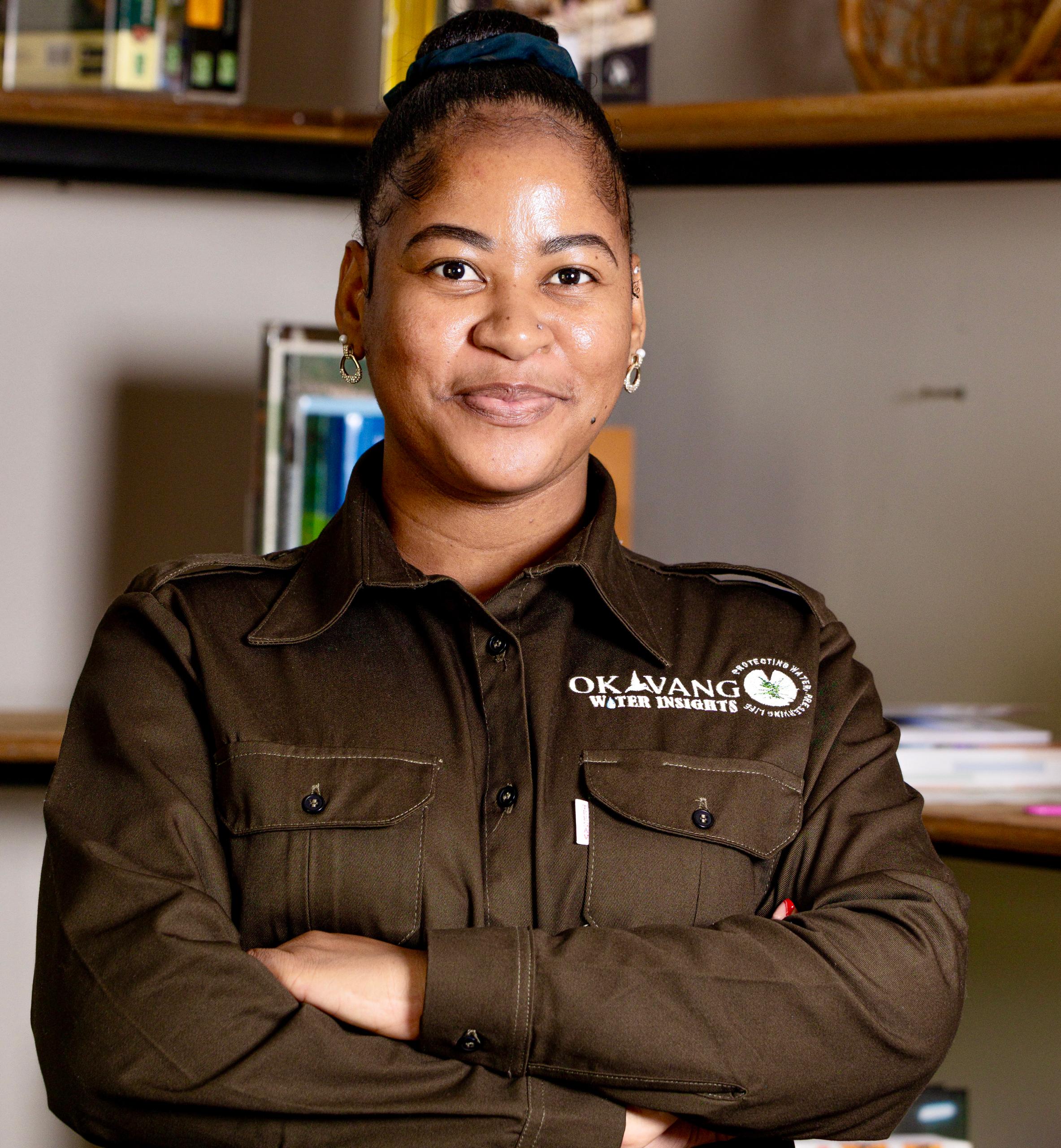 Smiling woman in brown uniform, arms crossed, standing in an office