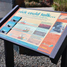A dashboard with various text about the rock garden stands in the dirt